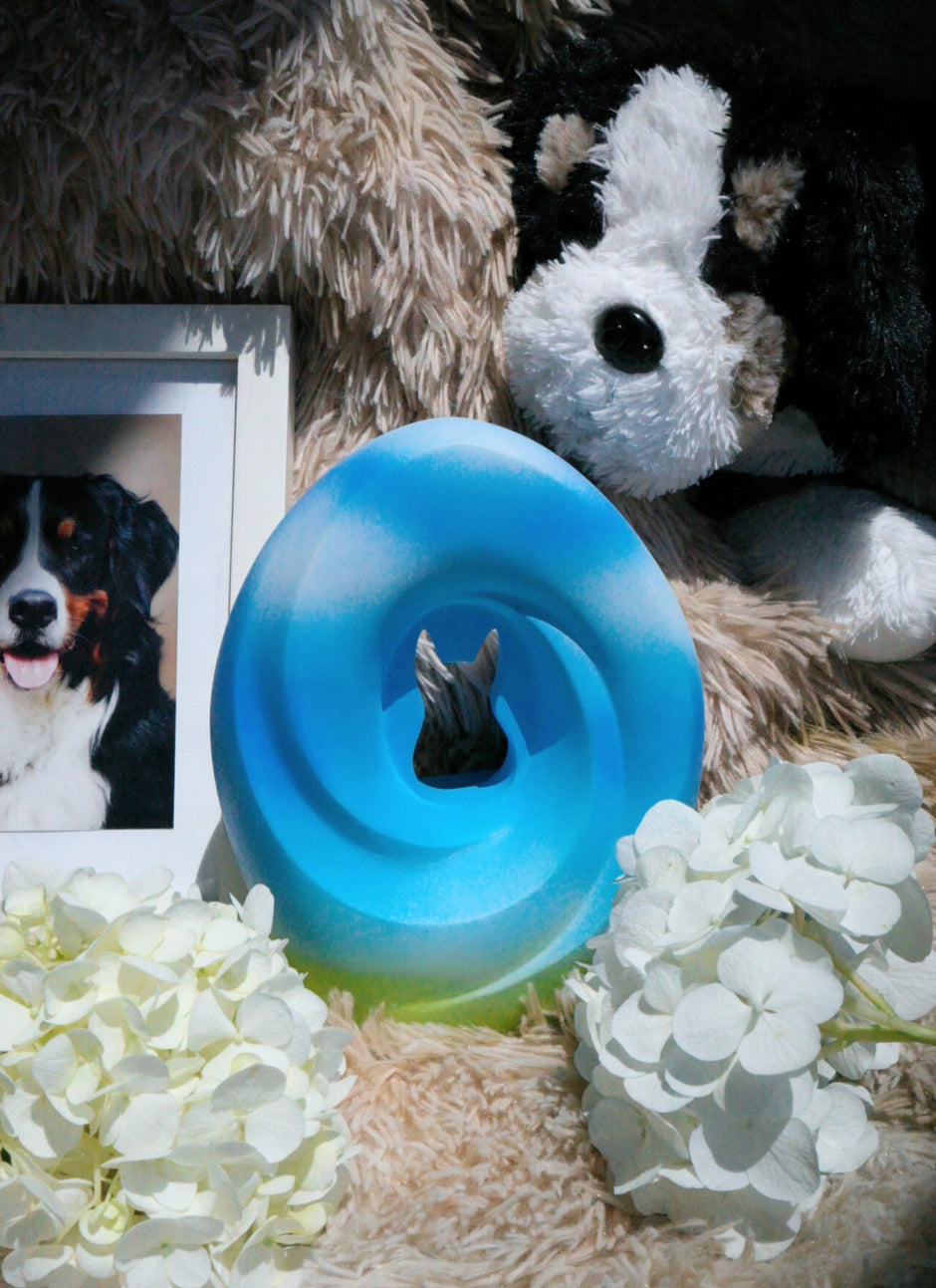 The Meadow Song Pet Urn surrounded by white flowers and a pet photo, placed in a cozy and serene memorial setting.
