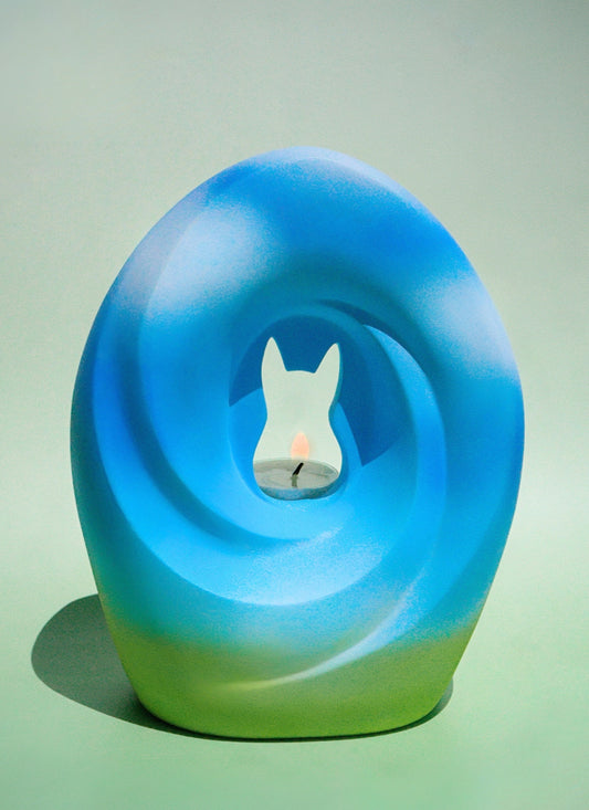 The Meadow Song Pet Urn featuring a modern design with a cat silhouette carved into a circular blue and green urn, inspired by serene meadows.